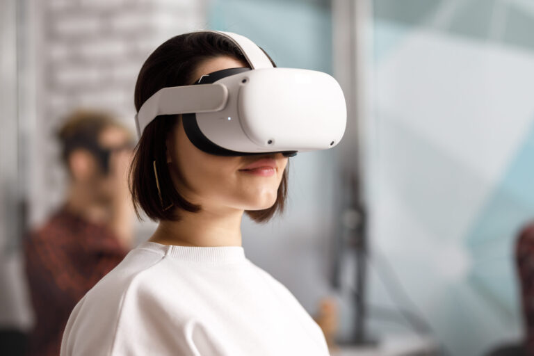 Team of four creative engineers working with virtual reality, young woman testing VR glasses or goggles sitting in the office room